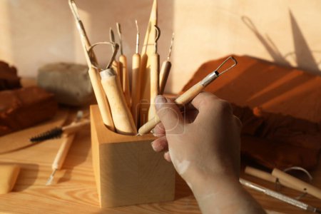 Frau nimmt in Werkstatt Ton-Bastelwerkzeug aus Holzhalter, Nahaufnahme