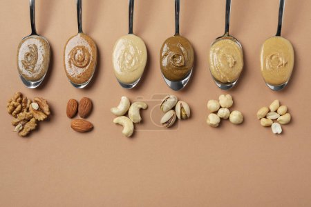 Photo for Tasty nut butters in spoons and raw nuts on light brown table, flat lay. Space for text - Royalty Free Image