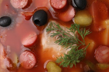 Meat solyanka soup with thin dry smoked sausages as background, top view