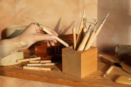 Woman taking clay crafting tool from wooden holder in workshop, closeup