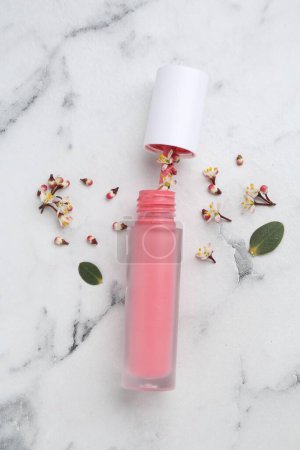 Rosafarbener Lipgloss, Blüten und grüne Blätter auf weißem Marmortisch, flache Lage