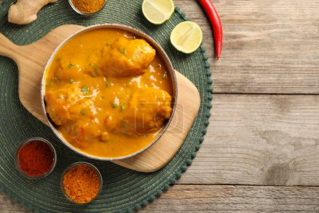 Tasty chicken curry and ingredients on wooden table, flat lay. Space for text