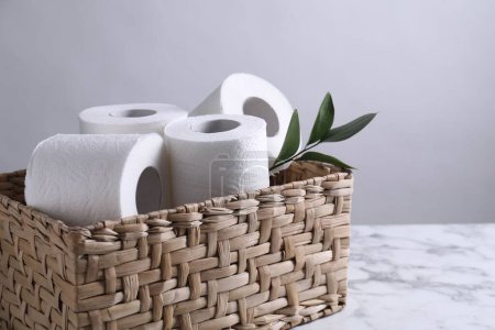 Téléchargez les photos : Rouleaux de papier toilette et feuilles vertes dans un panier en osier sur une table en marbre blanc, espace pour le texte - en image libre de droit
