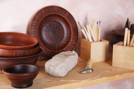 Conjunto de diferentes herramientas de elaboración y platos de arcilla en estante de madera en taller