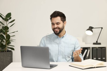 Foto de Hombre joven que tiene chat de vídeo a través de ordenador portátil en la mesa en el interior - Imagen libre de derechos
