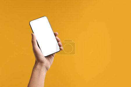 Mann hält Smartphone mit leerem Bildschirm auf gelbem Hintergrund, Nahaufnahme. Mockup für Design