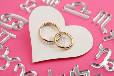Foto de Signos del zodíaco, corazón y anillos de boda sobre fondo rosa, primer plano - Imagen libre de derechos
