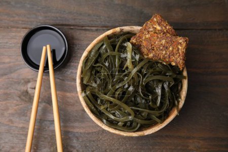 Tasty seaweed salad in bowl served on wooden table, flat lay