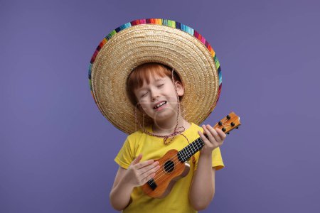 Lindo chico en sombrero mexicano tocando ukelele y cantando sobre fondo violeta, espacio para texto
