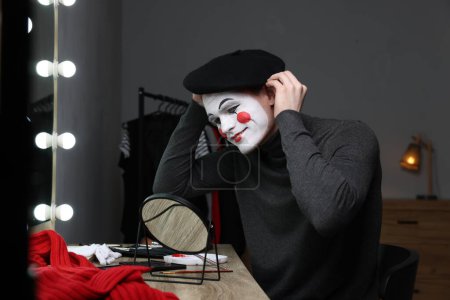 Mime artist putting on beret near mirror in dressing room