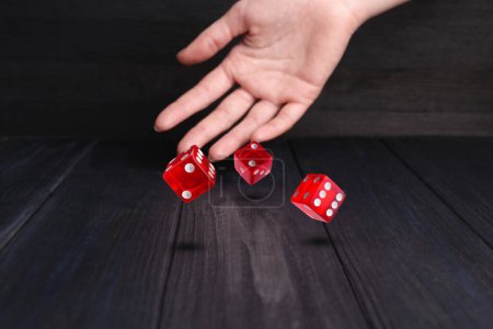 Woman throwing red dice on black wooden table, closeup