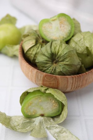Tomates verdes frescos con cáscara en un tazón sobre una mesa ligera, primer plano