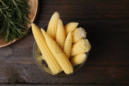 Tasty fresh yellow baby corns in glass on wooden table, top view