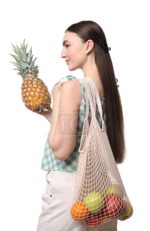 Téléchargez les photos : Femme avec sac à ficelle de fruits frais tenant l'ananas sur fond blanc - en image libre de droit