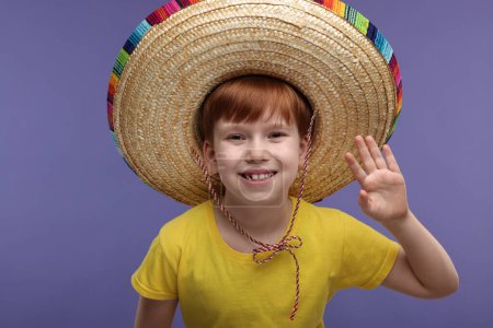 Lindo chico en sombrero mexicano saludando con un saludo sobre fondo violeta