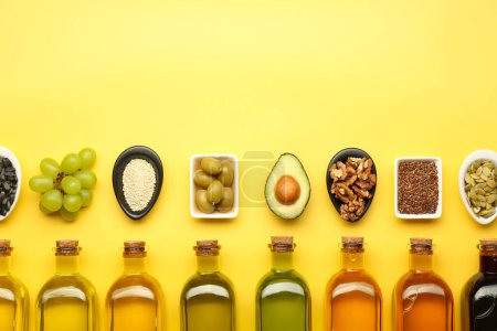 Foto de Grasas vegetales. Diferentes aceites en botellas de vidrio e ingredientes en la mesa amarilla, puesta plana. Espacio para texto - Imagen libre de derechos