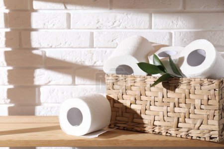 Téléchargez les photos : Rouleaux de papier hygiénique dans un panier en osier et feuilles vertes sur une étagère en bois contre un mur de briques blanches - en image libre de droit