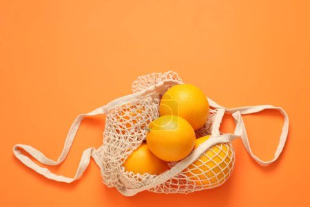 Téléchargez les photos : Sac à ficelle avec des oranges fraîches sur fond de couleur, vue de dessus. Espace pour le texte - en image libre de droit
