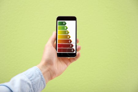 Foto de Calificación de eficiencia energética en la pantalla del teléfono inteligente. Dispositivo de sujeción del hombre sobre fondo verde claro, primer plano - Imagen libre de derechos
