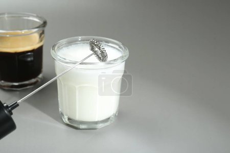 Mini mixer (milk frother), whipped milk and coffee in glasses on grey background, closeup. Space for text