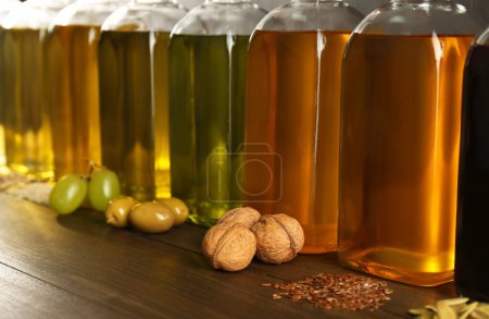 Foto de Grasas vegetales. Diferentes aceites en botellas de vidrio e ingredientes en mesa de madera, primer plano - Imagen libre de derechos