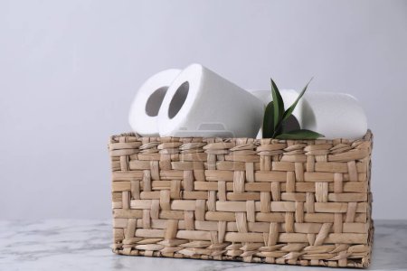 Téléchargez les photos : Rouleaux de papier toilette et feuilles vertes dans un panier en osier sur une table en marbre blanc - en image libre de droit