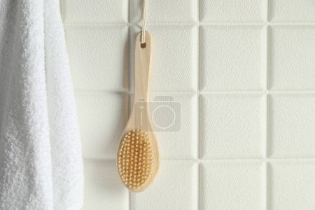 Accesorios de baño. Cepillo de bambú y toalla de rizo en la pared de azulejos blancos, espacio para el texto