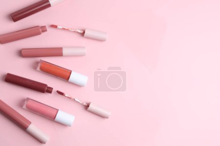 Foto de Diferentes glosas de labios y aplicadores sobre fondo rosa, plano laico. Espacio para texto - Imagen libre de derechos