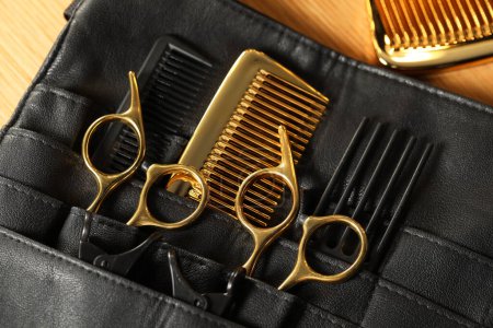 Hairdresser tools. Professional scissors and combs in leather organizer on wooden table, top view