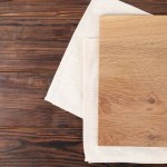 Cutting board and napkin on wooden table, top view. Space for text