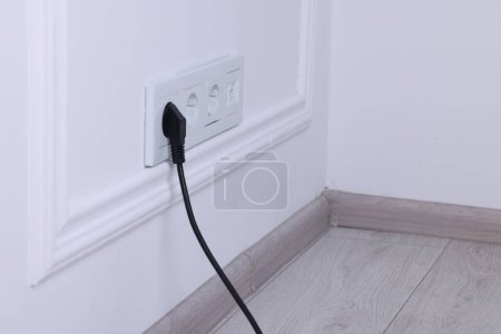 Power sockets and electric plug on white wall, space for text