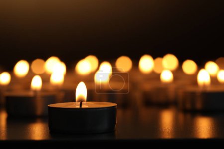 Brennende Kerzen auf dunkler Oberfläche vor schwarzem Hintergrund, Nahaufnahme. Raum für Text