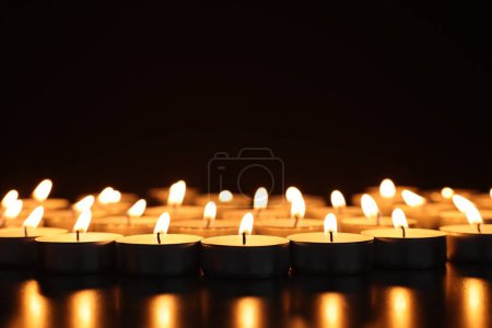 Téléchargez les photos : Brûler des bougies sur une surface sombre sur fond noir, gros plan. Espace pour le texte - en image libre de droit