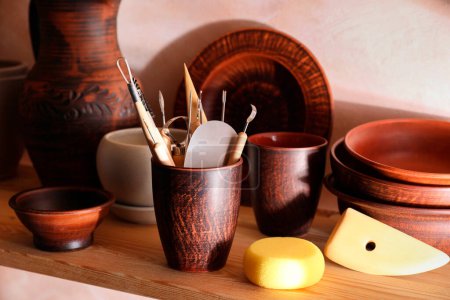 Foto de Conjunto de diferentes herramientas de elaboración y platos de arcilla en estante de madera en taller - Imagen libre de derechos