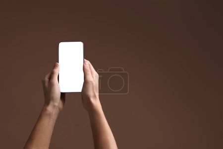 Mann hält Smartphone mit leerem Bildschirm auf braunem Hintergrund, Nahaufnahme. Mockup für Design