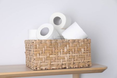 Téléchargez les photos : Rouleaux de papier toilette dans un panier en osier sur une table en bois près d'un mur blanc - en image libre de droit
