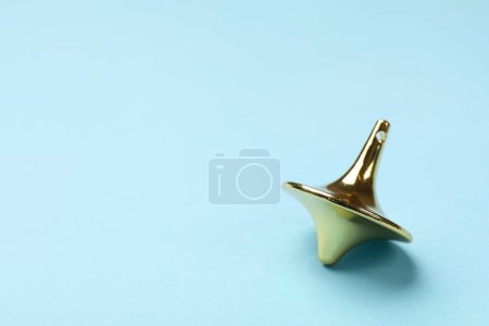 One golden spinning top on light blue background, closeup. Space for text