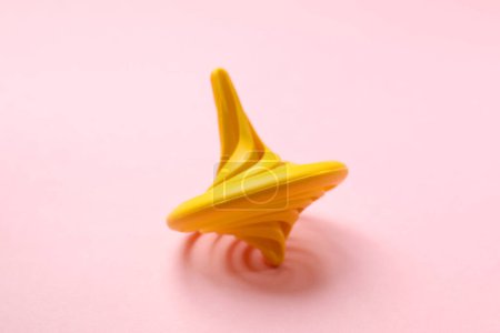 Yellow spinning top on pink background, closeup