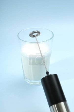 Mini mezclador (espuma de leche) y leche batida en vaso sobre fondo azul claro