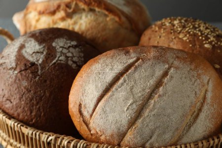 Wicker basket with different types of fresh bread against grey background, closeup
