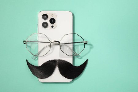 Téléchargez les photos : Moustache artificielle, smartphone et lunettes sur fond turquoise, vue de dessus. Espace pour le texte - en image libre de droit