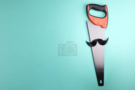 Téléchargez les photos : Visage d'homme fait de moustache artificielle et scie à main sur fond bleu clair, vue de dessus. Espace pour le texte - en image libre de droit