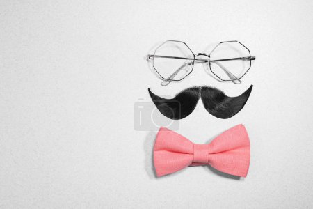 Téléchargez les photos : Visage d'homme fait de moustache artificielle, noeud papillon et lunettes sur fond gris clair, vue de dessus. Espace pour le texte - en image libre de droit