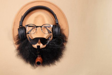 Téléchargez les photos : Visage d'homme fait de moustache artificielle, barbe, lunettes et chapeau sur fond beige, vue de dessus. Espace pour le texte - en image libre de droit