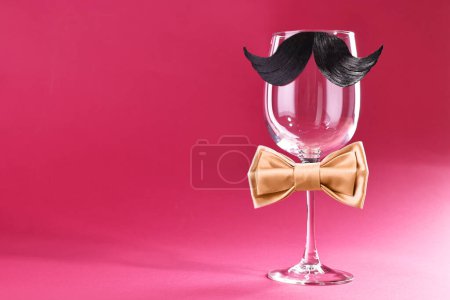 Téléchargez les photos : Visage d'homme fait de moustache artificielle, noeud papillon et verre de vin sur fond cramoisi. Espace pour le texte - en image libre de droit