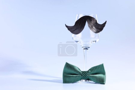 Téléchargez les photos : Visage d'homme fait de moustache artificielle, noeud papillon et verre à vin sur fond bleu clair. Espace pour le texte - en image libre de droit