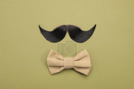 Téléchargez les photos : Moustache artificielle et noeud papillon sur fond kaki, vue de dessus - en image libre de droit