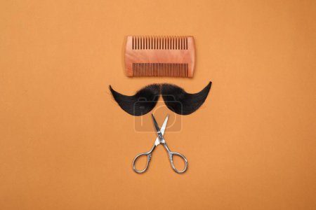 Téléchargez les photos : Moustache artificielle, peigne et ciseaux sur fond orange, vue de dessus - en image libre de droit