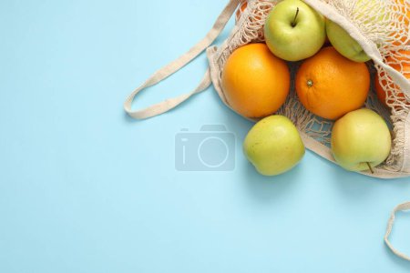Téléchargez les photos : Sac à ficelle avec pommes et oranges fraîches sur fond bleu clair, vue de dessus. Espace pour le texte - en image libre de droit