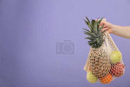 Téléchargez les photos : Femme avec sac à ficelle de fruits frais sur fond violet, gros plan. Espace pour le texte - en image libre de droit